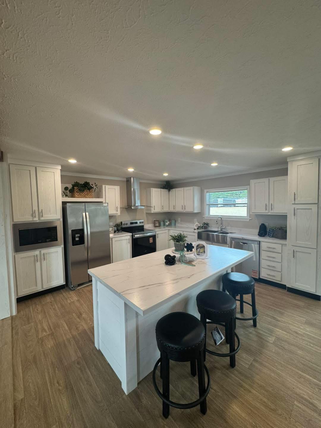 Modern kitchen with white cabinets, stainless steel appliances, and a central island with barstools. Wood flooring adds warmth to the bright space.