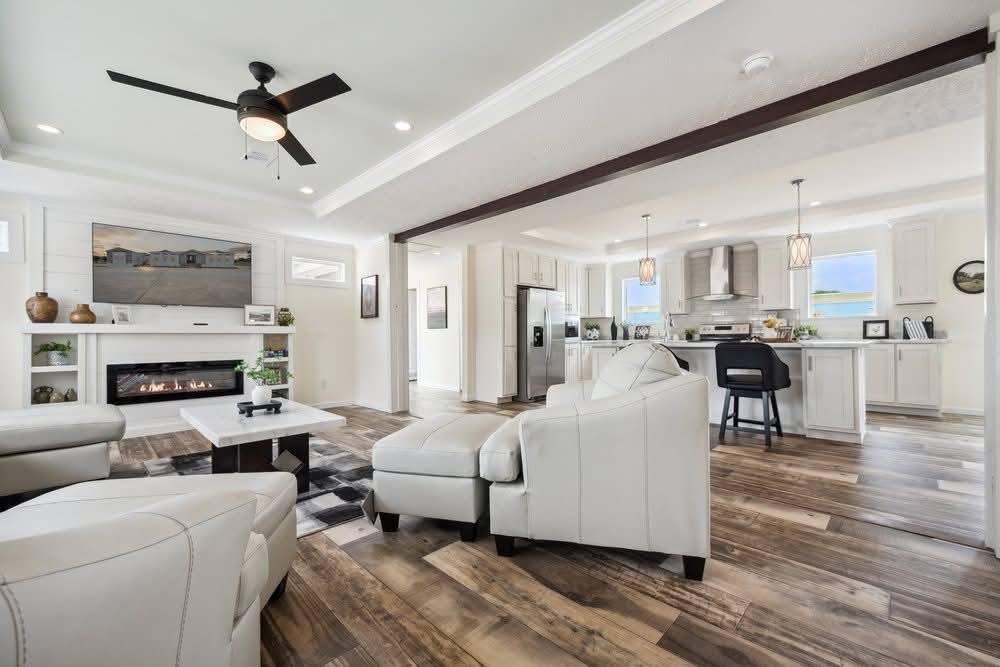 Modern open-plan living room with white furniture and wood flooring, connected to a sleek kitchen. A cozy atmosphere with neutral tones and soft lighting.