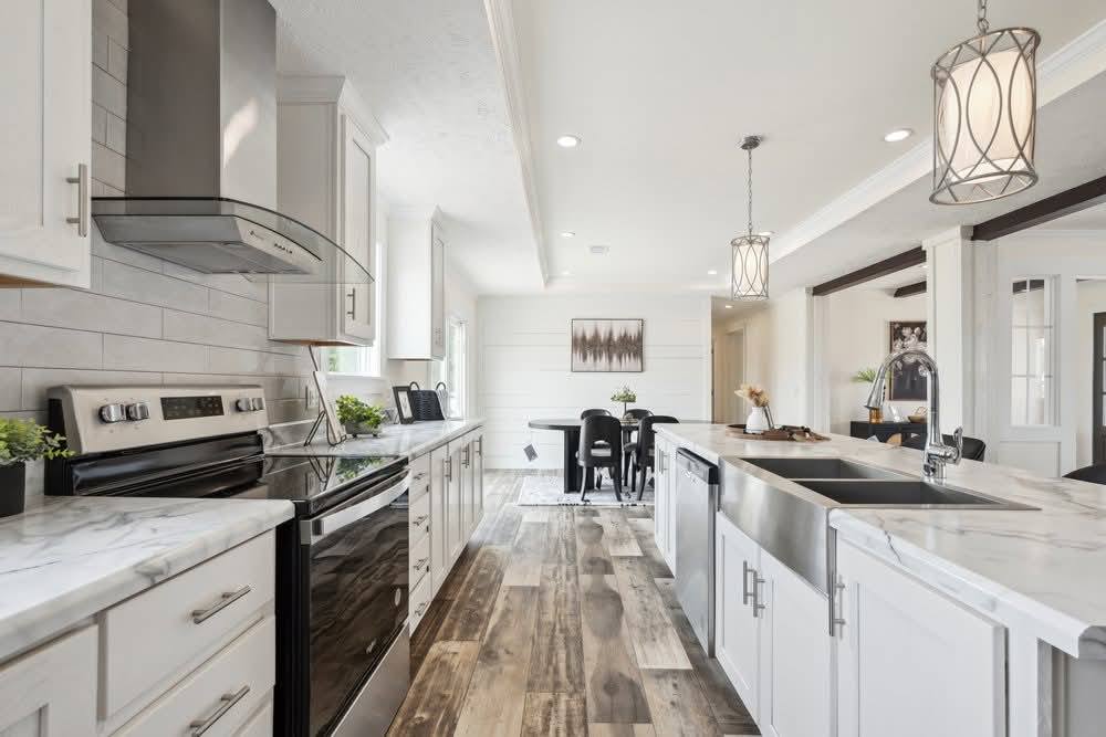 Sleek modern kitchen with white cabinets, stainless steel appliances, and marble countertops. Warm wooden floors lead to a dining area with a black table.
