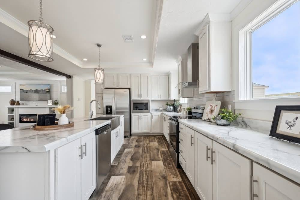 Bright, modern kitchen with white cabinets, marble countertops, and wood flooring. Stainless steel appliances. Large window and elegant pendant lights.