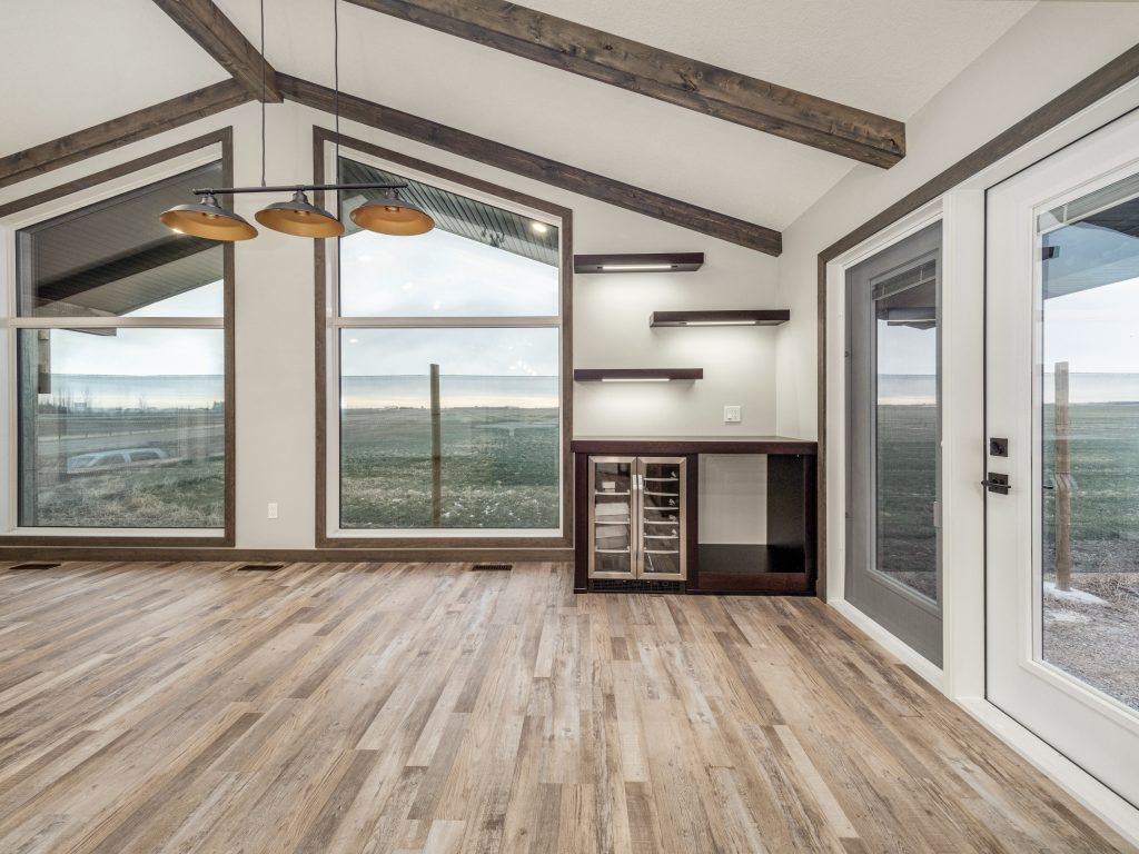 Spacious room with large windows overlooking a scenic landscape. Features wooden floors, modern pendant lights, and a sleek bar area. Cozy and inviting.