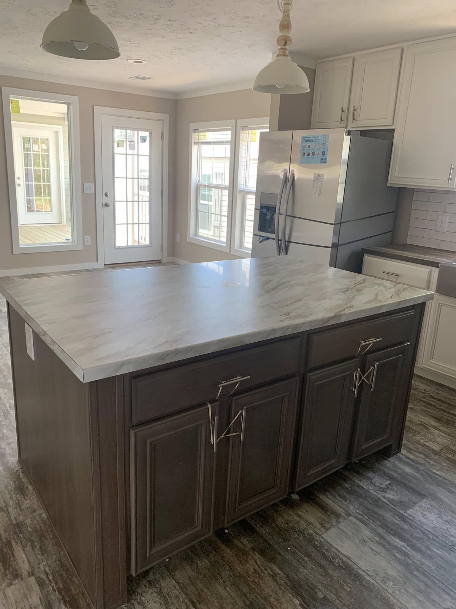 Modern kitchen with large marble island, dark wood cabinets, stainless steel fridge. Sunlit through glass doors, creating an inviting atmosphere.
