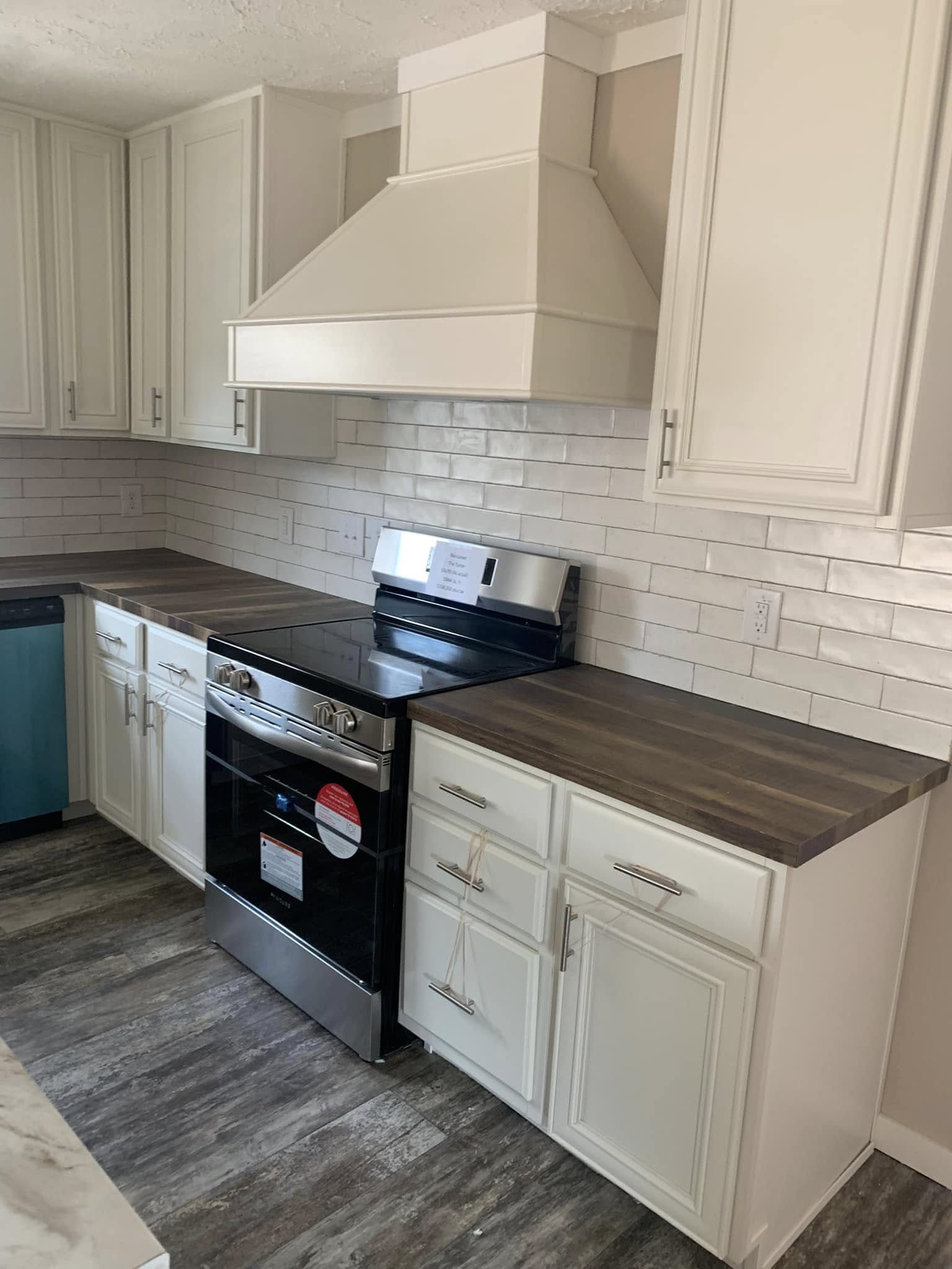 Modern kitchen with white cabinets, dark wood countertops, and a stainless steel oven. The backsplash features white subway tiles, and the floor is a gray wood laminate.