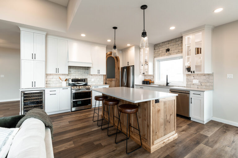 Spacious kitchen with a modern-rustic style. Features a large island with wooden base, white cabinets, stainless steel appliances, and pendant lights.