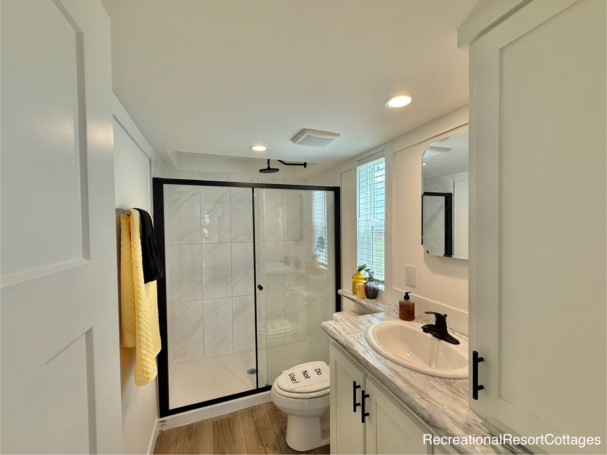 Modern bathroom with a sleek glass-enclosed shower, marble-topped vanity, and bright white cabinetry. Yellow towel and decorative items add warmth.