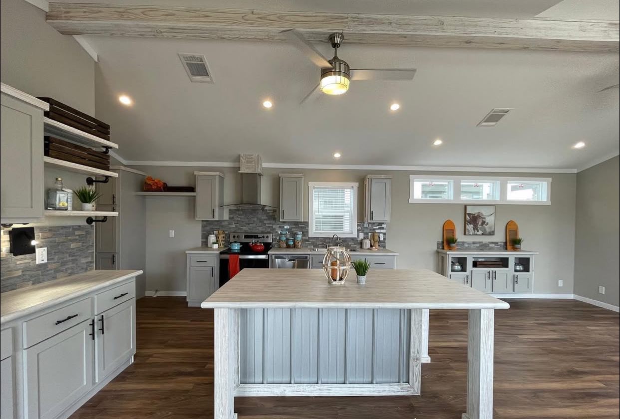 Spacious modern kitchen with light gray cabinets, wood flooring, and a central island. Warm lighting and decor create a cozy, inviting atmosphere.