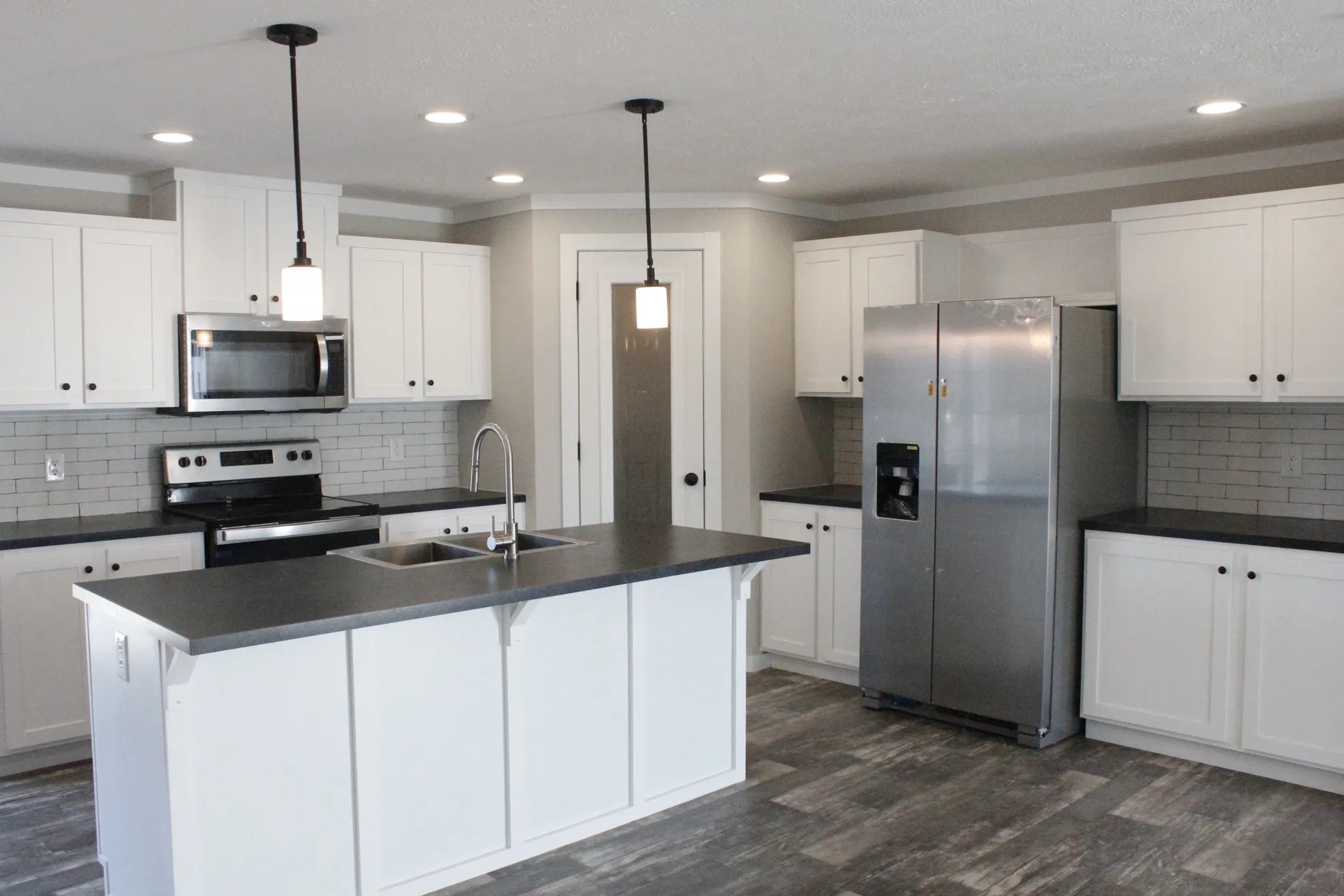 Modern kitchen with white cabinets, gray countertops, stainless steel appliances, and pendant lights. Central island with a sink, exuding a sleek, clean vibe.