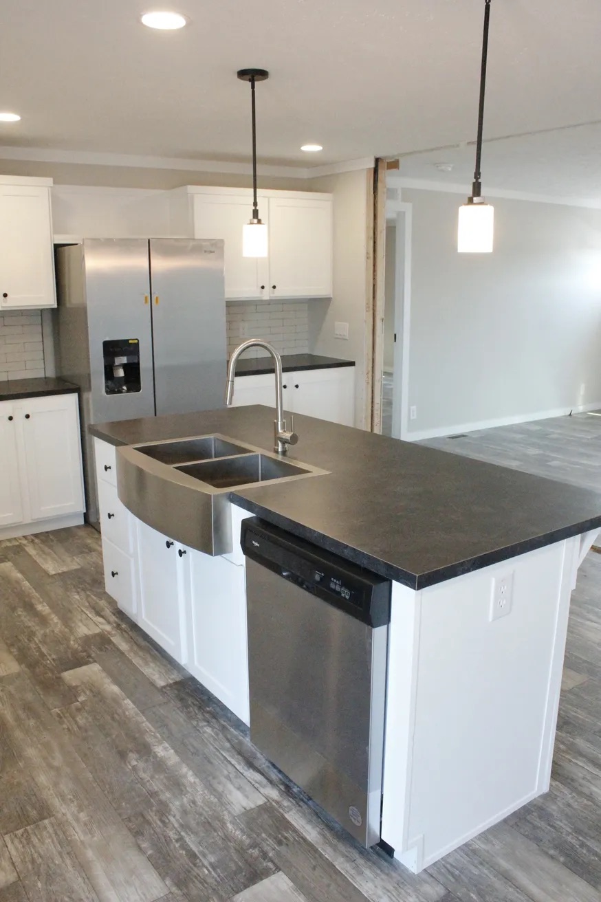 Modern kitchen with white cabinets, stainless steel appliances, and a black countertop island with a double sink. Warm lighting creates an inviting feel.