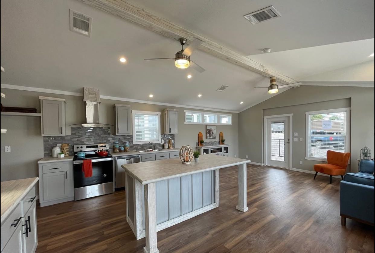 Spacious modern kitchen with wooden flooring, white cabinets, and central island. Ceiling fans and recessed lighting create an airy, inviting atmosphere.