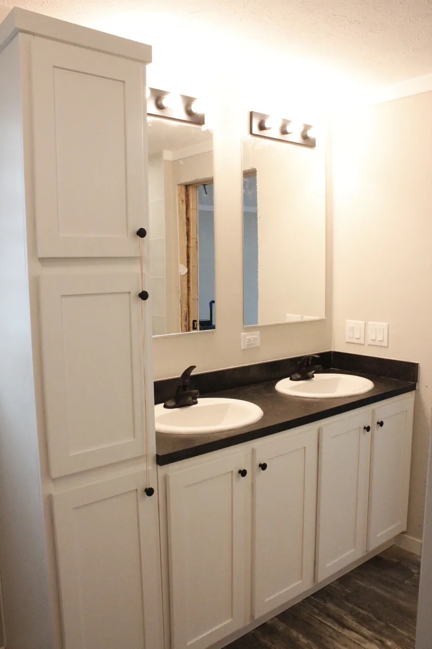 A modern bathroom features a double sink vanity with black countertops and bronze faucets. Two mirrors and bright lights enhance the clean, minimalist design.