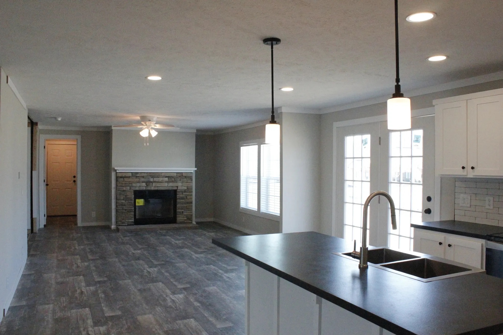 Modern open-concept kitchen and living area with gray tile floors, a cozy fireplace, sleek dark countertops, pendant lighting, and large windows.