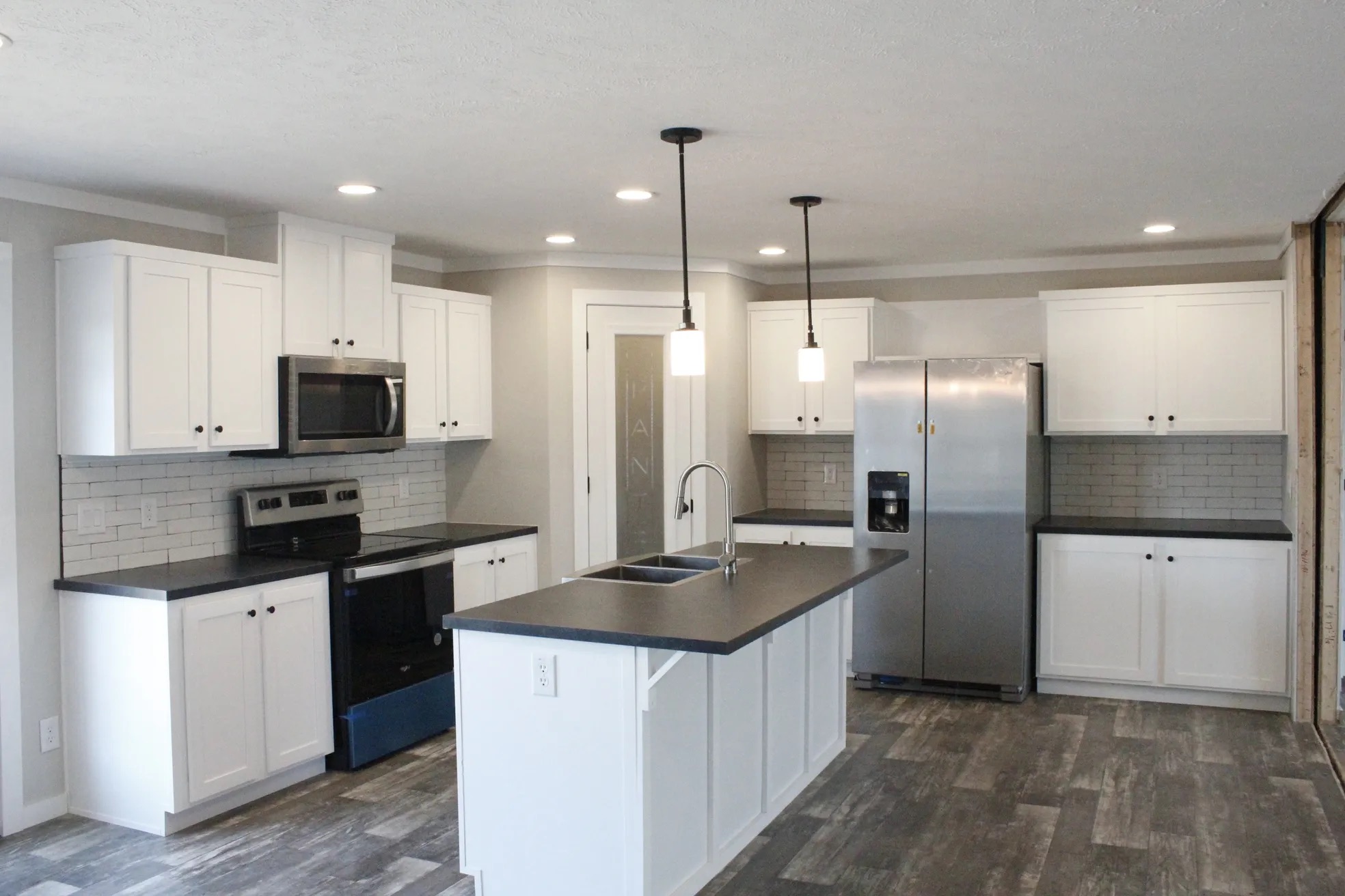 Modern kitchen with white cabinets, stainless steel appliances, and a central island with pendant lights. Gray tile flooring adds a sleek touch.