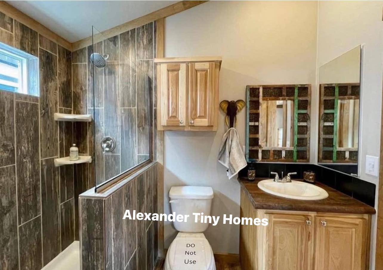 Bathroom in a tiny home features wood accents, a tiled shower, and a wooden cabinet above a toilet with a "Do Not Use" sign, conveying a rustic feel.