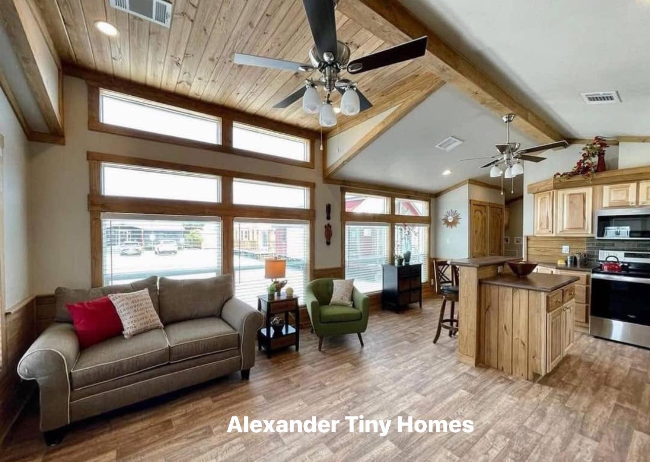Spacious tiny home interior with wooden accents, featuring a cozy sofa, armchair, and modern kitchen. Large windows provide ample natural light.