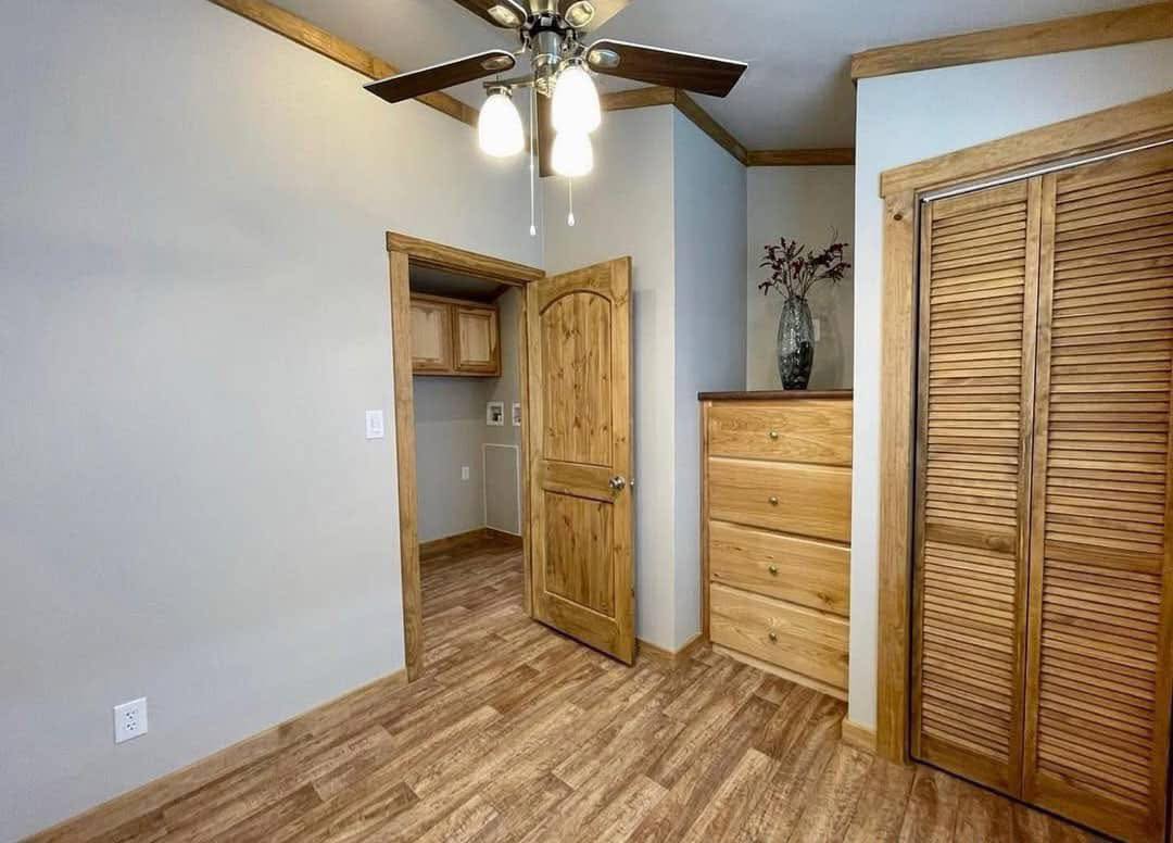 A cozy room featuring a wooden floor and natural wood accents. An open door reveals a small closet. A ceiling fan with lights adds warmth.