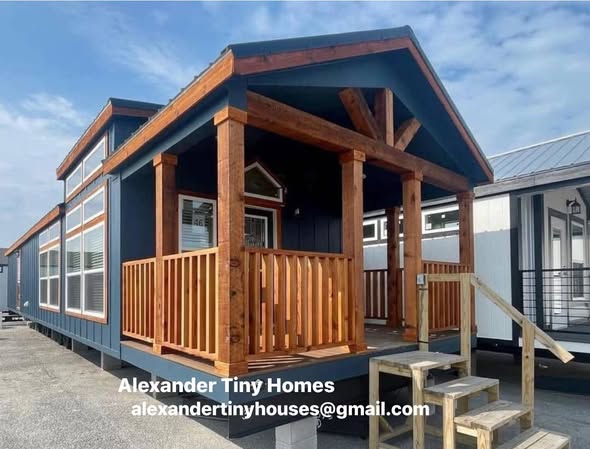 Modern tiny home with a wooden porch and blue exterior under a clear sky. Text reads: "Alexander Tiny Homes, alexandertinyhouses@gmail.com."