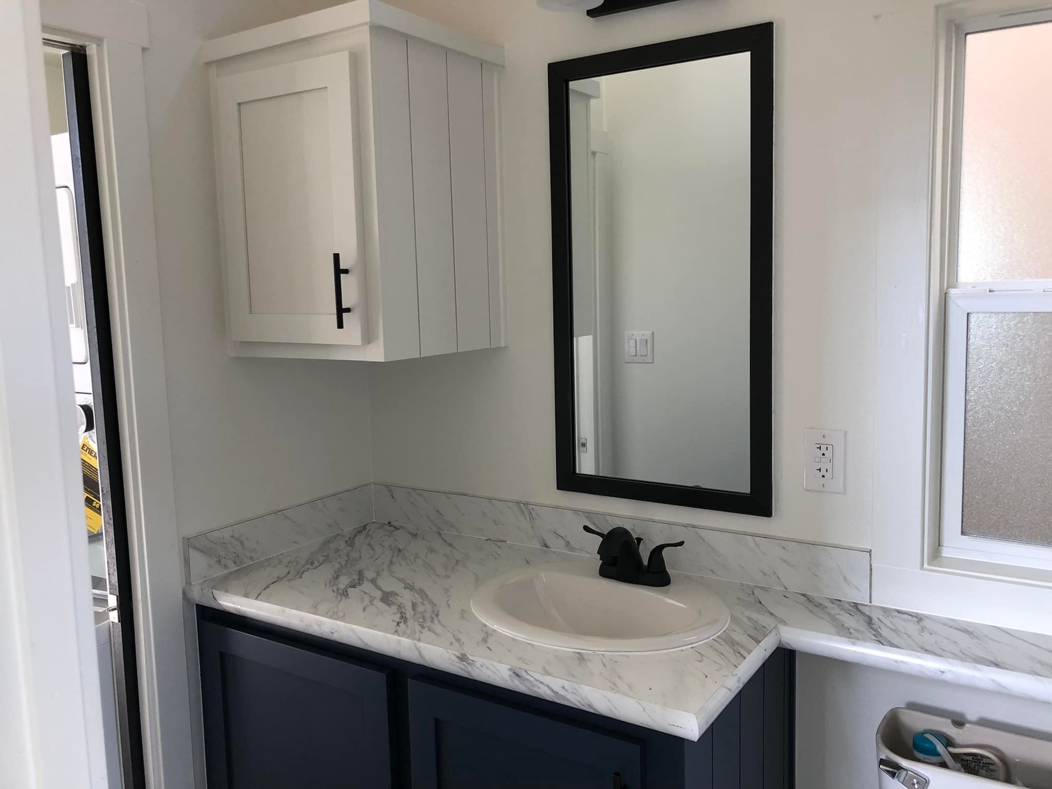 Small, modern bathroom with a white marble countertop and dark blue cabinets. Features a rectangular mirror and black faucet, evoking a sleek, clean vibe.