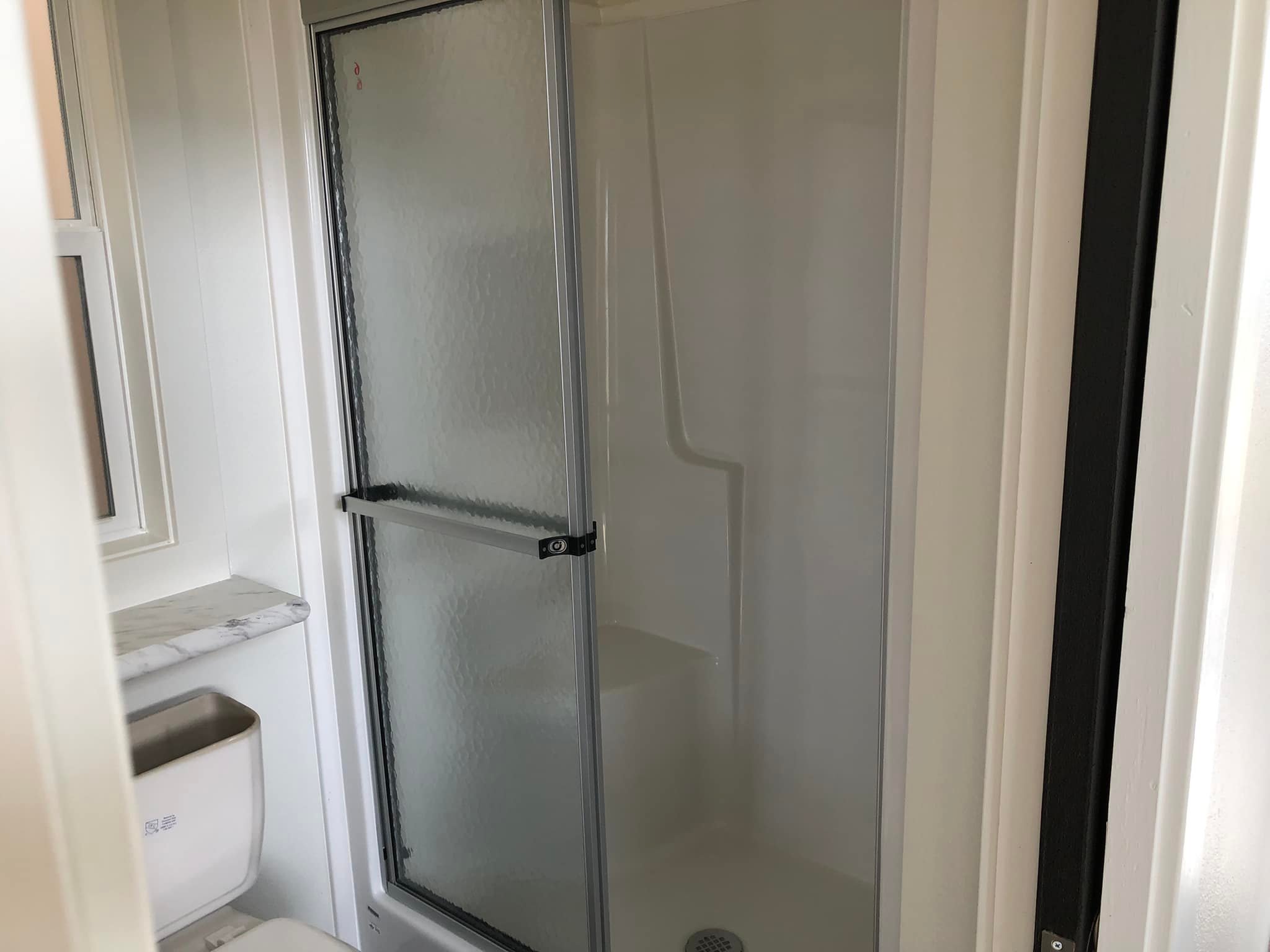 Compact bathroom with a frosted glass shower door. A small white toilet sits next to a marble countertop, creating a clean, minimalistic space.