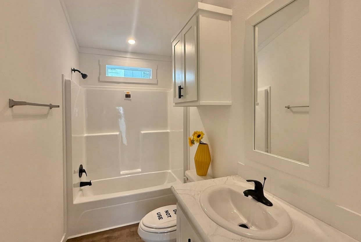 A bright, modern bathroom with white walls, a bathtub, and a sink with a black faucet. A yellow vase with flowers adds color, creating a fresh feel.