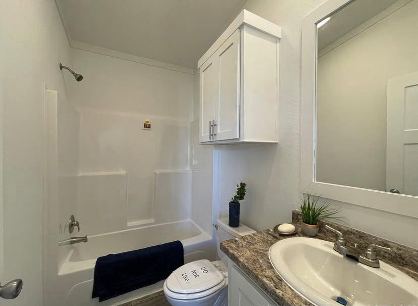 Small bathroom with a bathtub and shower, granite countertop, white cabinets, and a mirror. Decor includes a potted plant and navy towel.