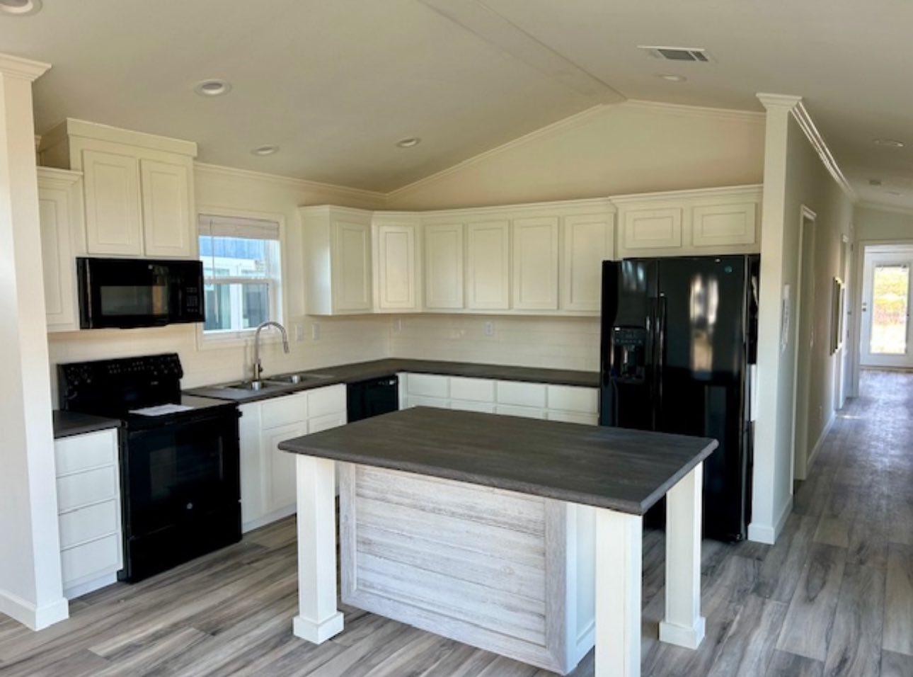 Spacious modern kitchen with white cabinets, black appliances, and a central island with a dark wood countertop. Light wood flooring creates an airy feel.