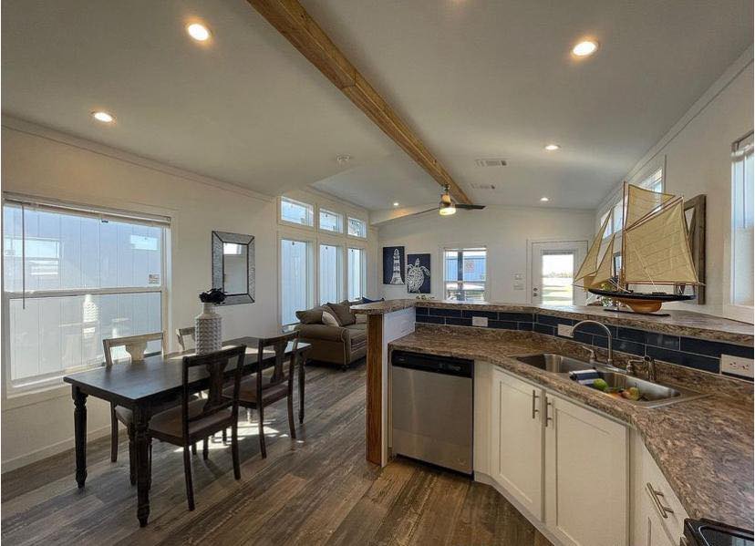 Modern open-plan kitchen and dining area with wood beam, sleek countertops, and a decorative ship model. Bright, airy atmosphere with large windows.