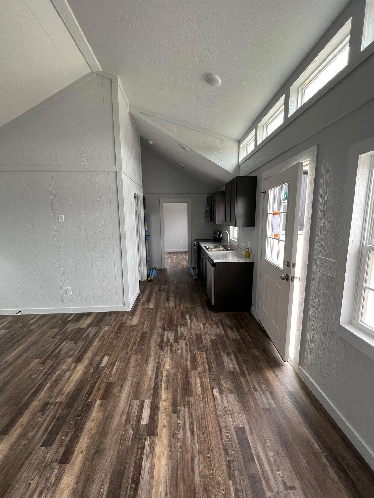 Bright modern kitchen with high ceilings, wood flooring, white walls, and dark cabinets. Sunlight streams through upper windows, enhancing openness.