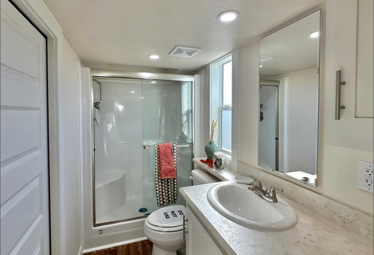 A sleek, modern bathroom featuring a glass shower, a white ceramic sink on a marble countertop, and a decorated counter with a vase and towel.