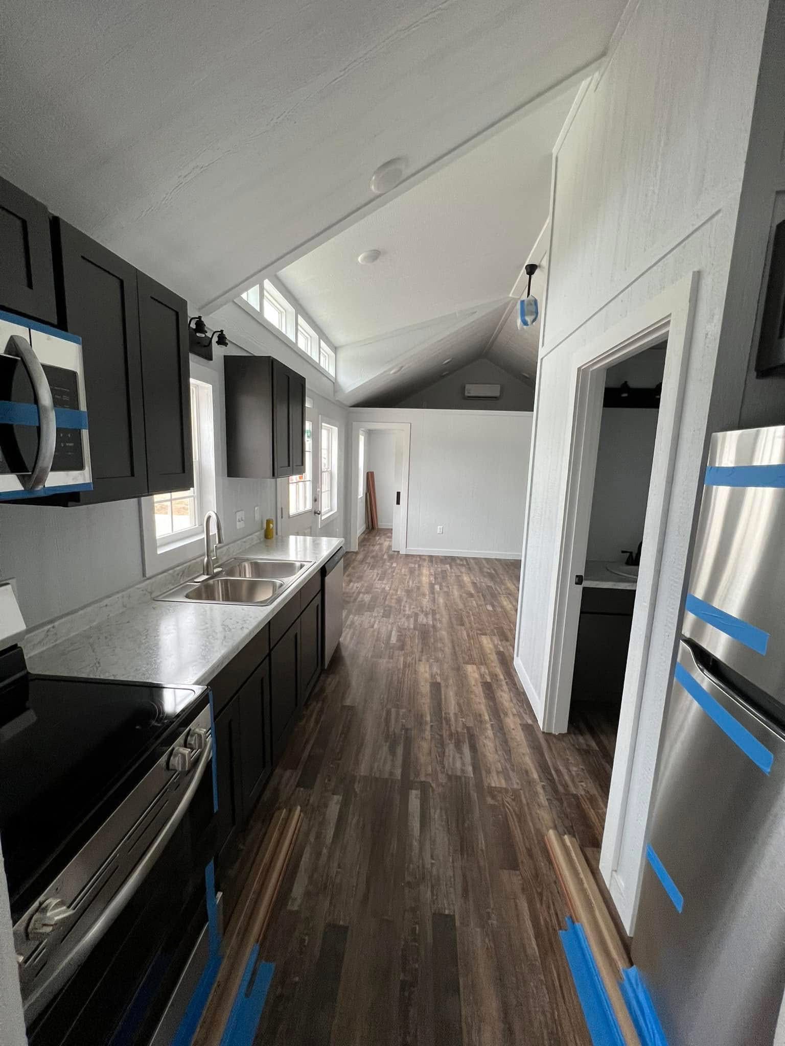Modern kitchen with high vaulted ceiling, dark cabinets, and wood-look flooring. Natural light streams through windows, creating a bright, airy feel.