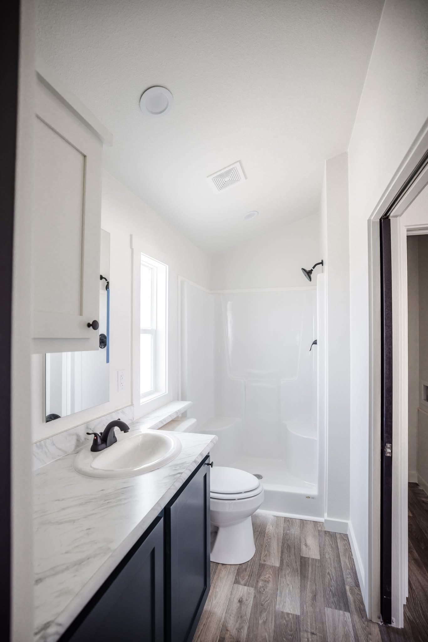Bright and minimalistic bathroom with white walls, a wood-textured floor, dark cabinetry, a white marble countertop, and a shower-tub combo.