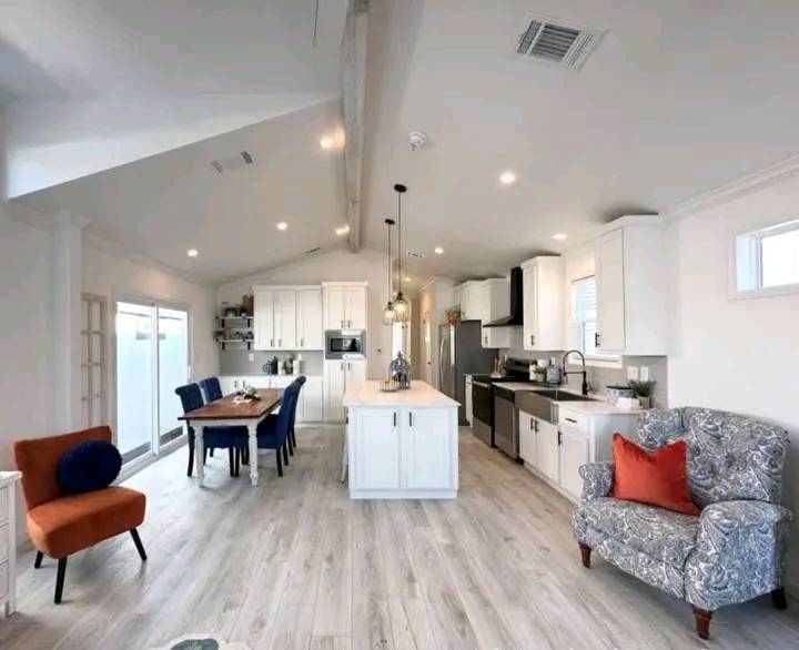 Spacious, modern open-plan kitchen and dining area with white cabinetry, an island, and a wooden table. Cozy accents include blue chairs, an orange chair, and a patterned armchair.