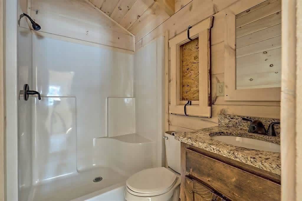 Rustic bathroom with wood-paneled walls and ceiling, featuring a white shower, granite counter, wooden cabinet, and iron accents, creating a cozy atmosphere.