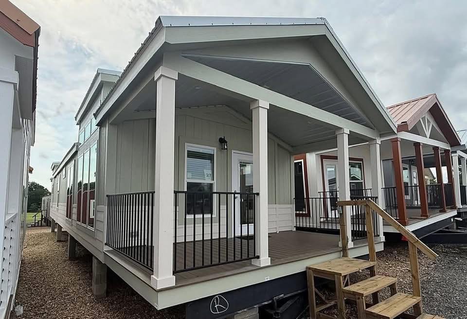 A row of modern tiny houses with front porches and metal roofs. The foreground house features a light exterior with black railings, creating a welcoming feel.