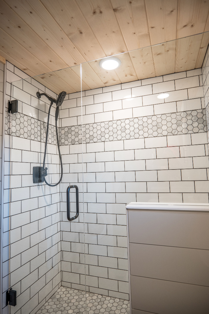 A modern shower with white subway tiles and a decorative hexagon tile stripe. It features a glass door and sleek black fixtures, creating a clean, elegant feel.