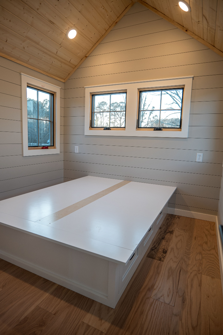 Cozy room with wooden walls and ceiling, featuring built-in bench storage and three small windows. Natural light creates a warm, inviting atmosphere.