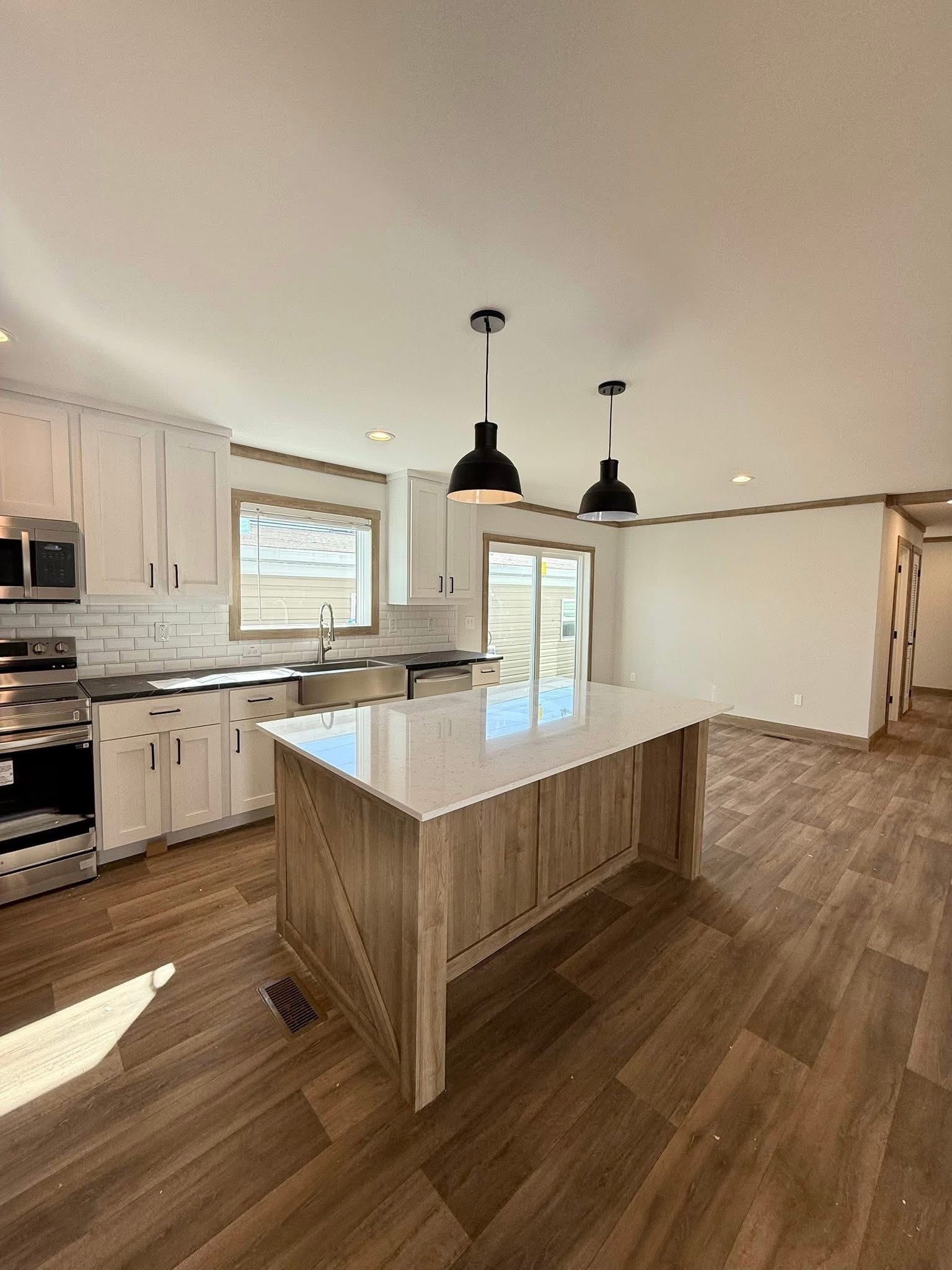 Modern kitchen with white cabinets, stainless steel appliances, and a wooden island with a white countertop. Two black pendant lights hang above.