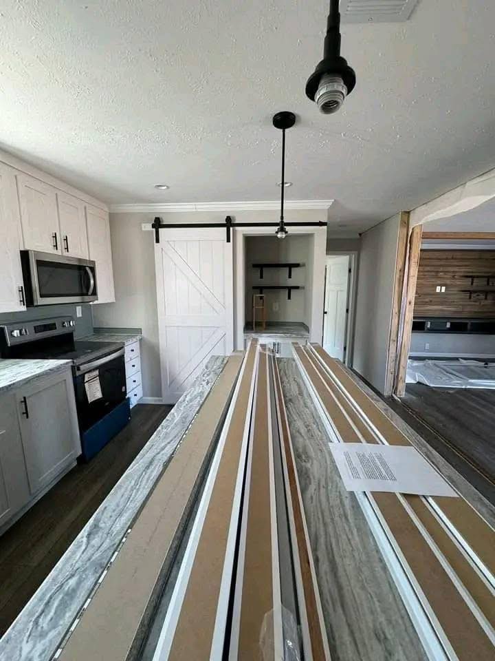 Modern kitchen with light cabinetry, a marble island, and pendant lights. Features a barn door and open shelving, creating a sleek, inviting atmosphere.