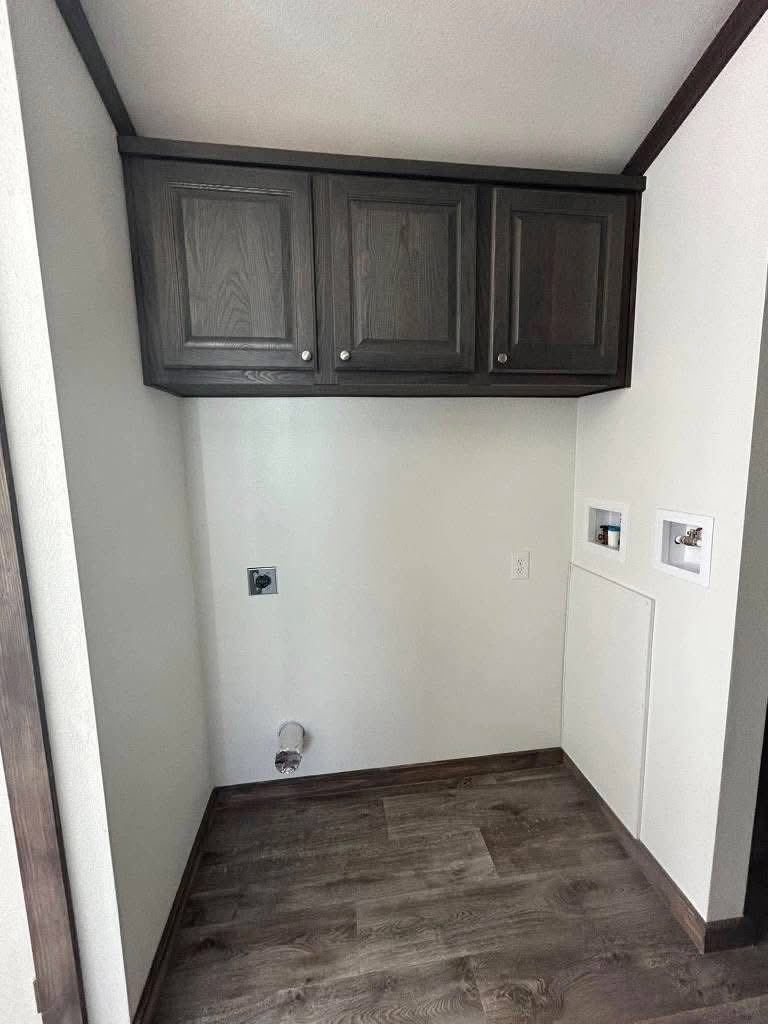Empty laundry room with dark wooden cabinets, a white wall, and plumbing fixtures for a washer and dryer. The floor is wood-patterned vinyl.