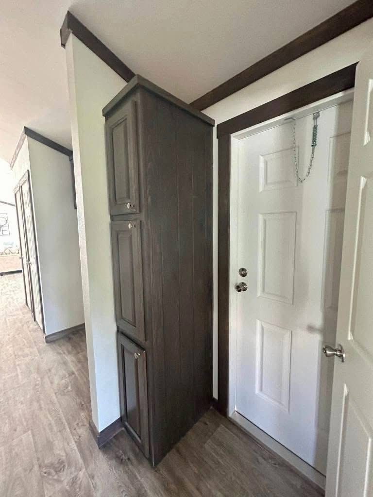 Tall, narrow dark wooden cabinet adjacent to a white door with a chain lock, set in a hallway with light-colored walls and wood flooring. Cozy atmosphere.