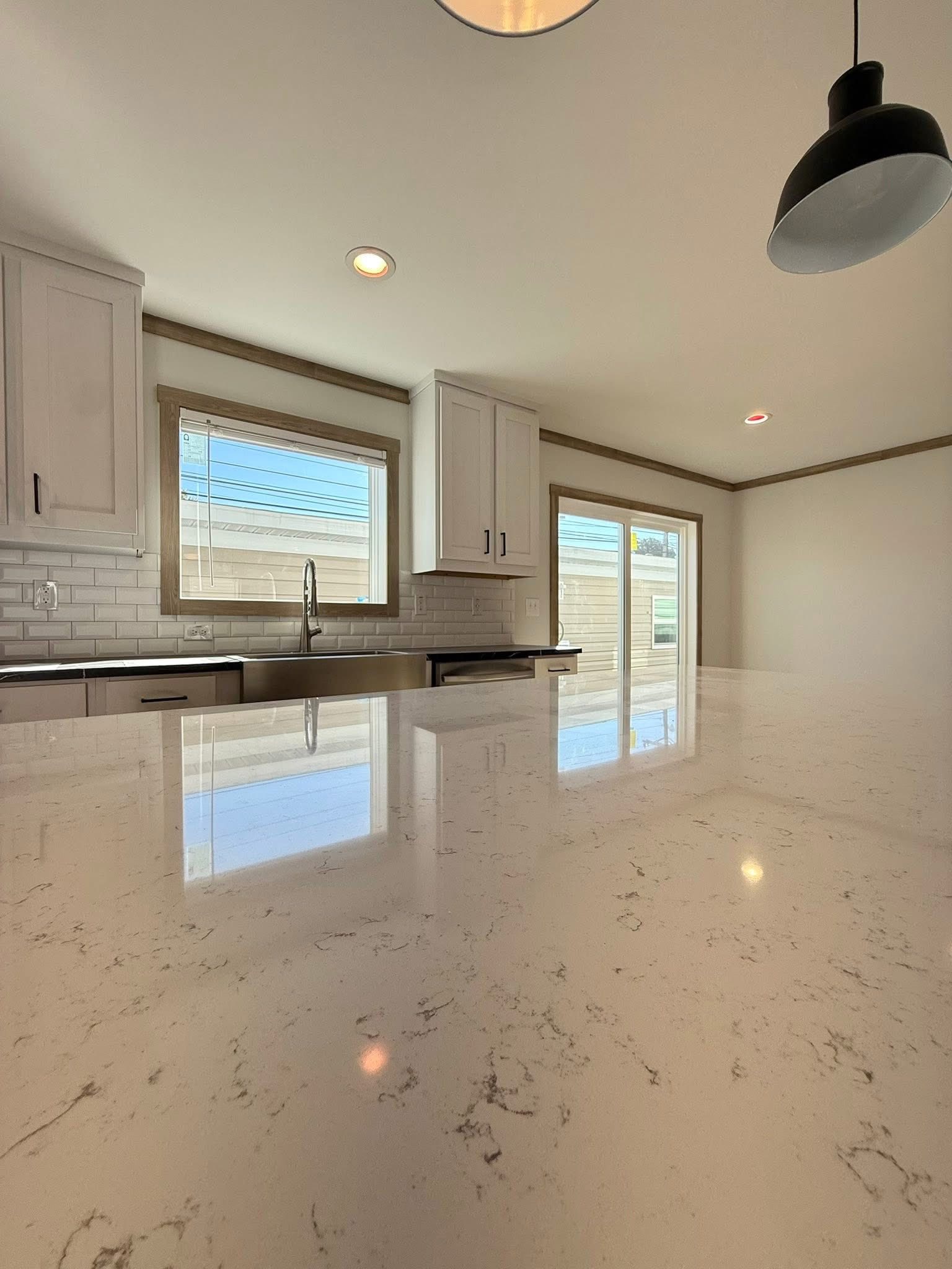 Sleek kitchen with glossy marble countertop, stainless steel sink, white cabinets, and subway tile backsplash. Sunlit, minimalist, modern ambiance.