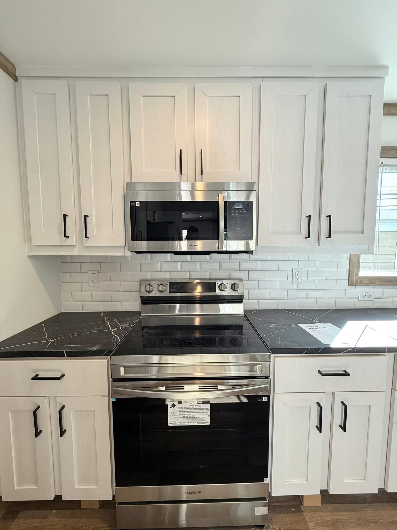 Modern kitchen with white cabinets, black marble countertops, and stainless steel appliances including a stove and microwave. Bright, clean, and sleek design.