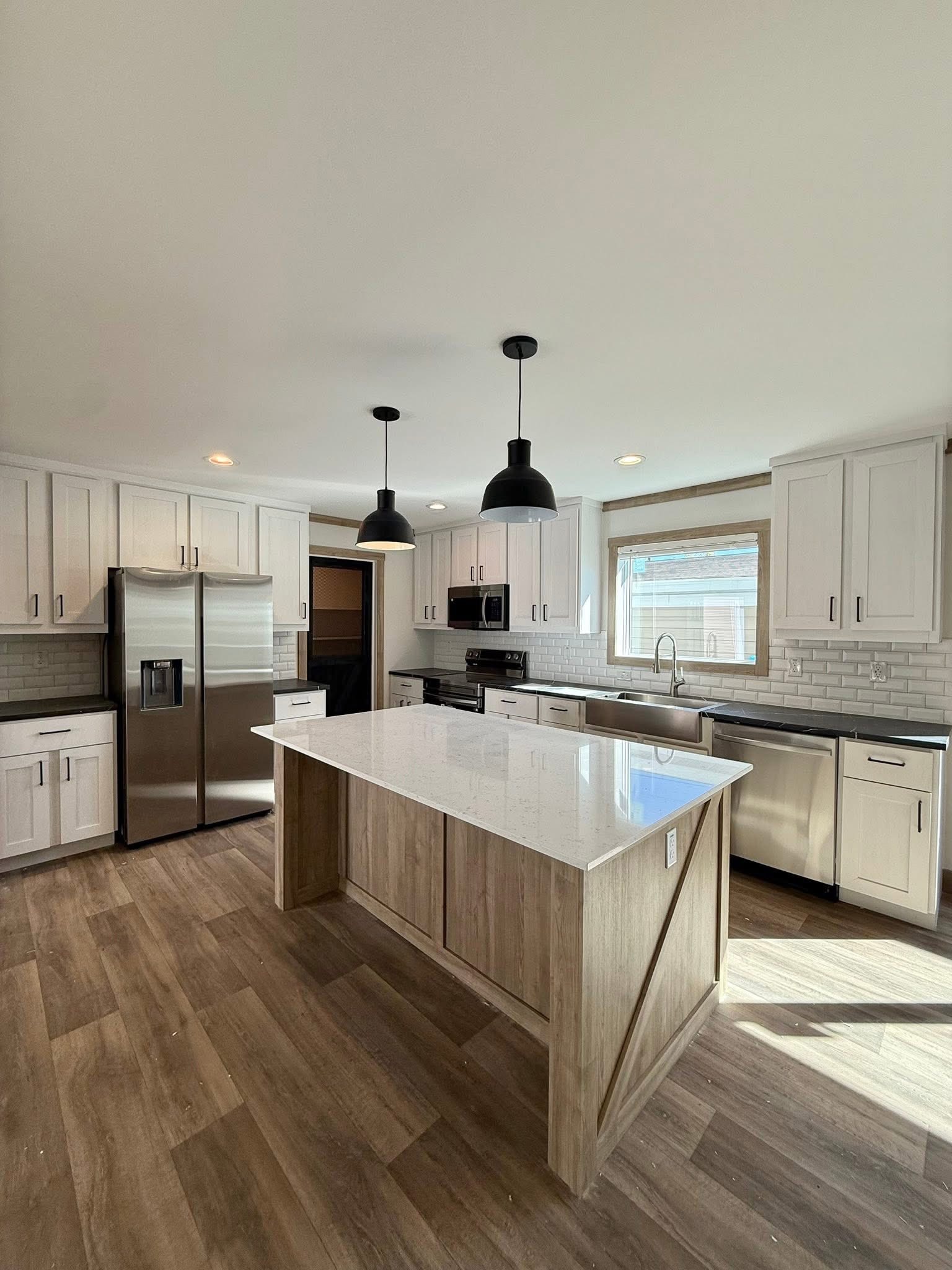 Modern kitchen with white cabinets and a marble island, featuring stainless steel appliances, wooden floor, and two black pendant lights.