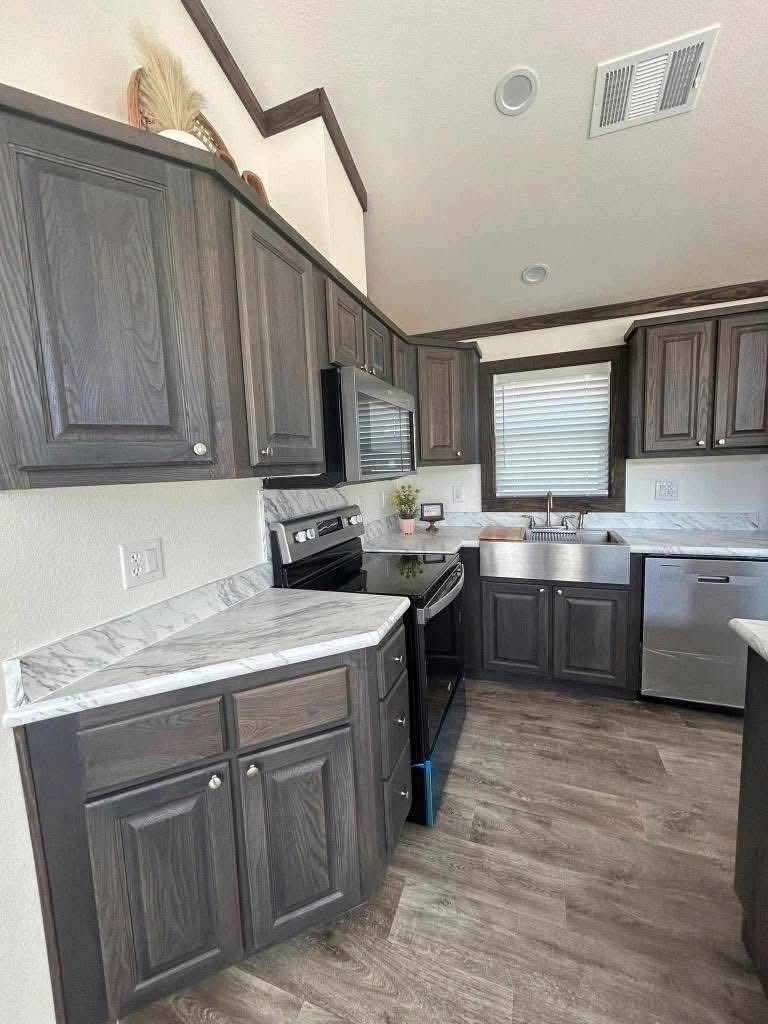 Modern kitchen with dark wood cabinets, marble countertops, stainless steel appliances, and a sink under a window. Warm, inviting atmosphere.