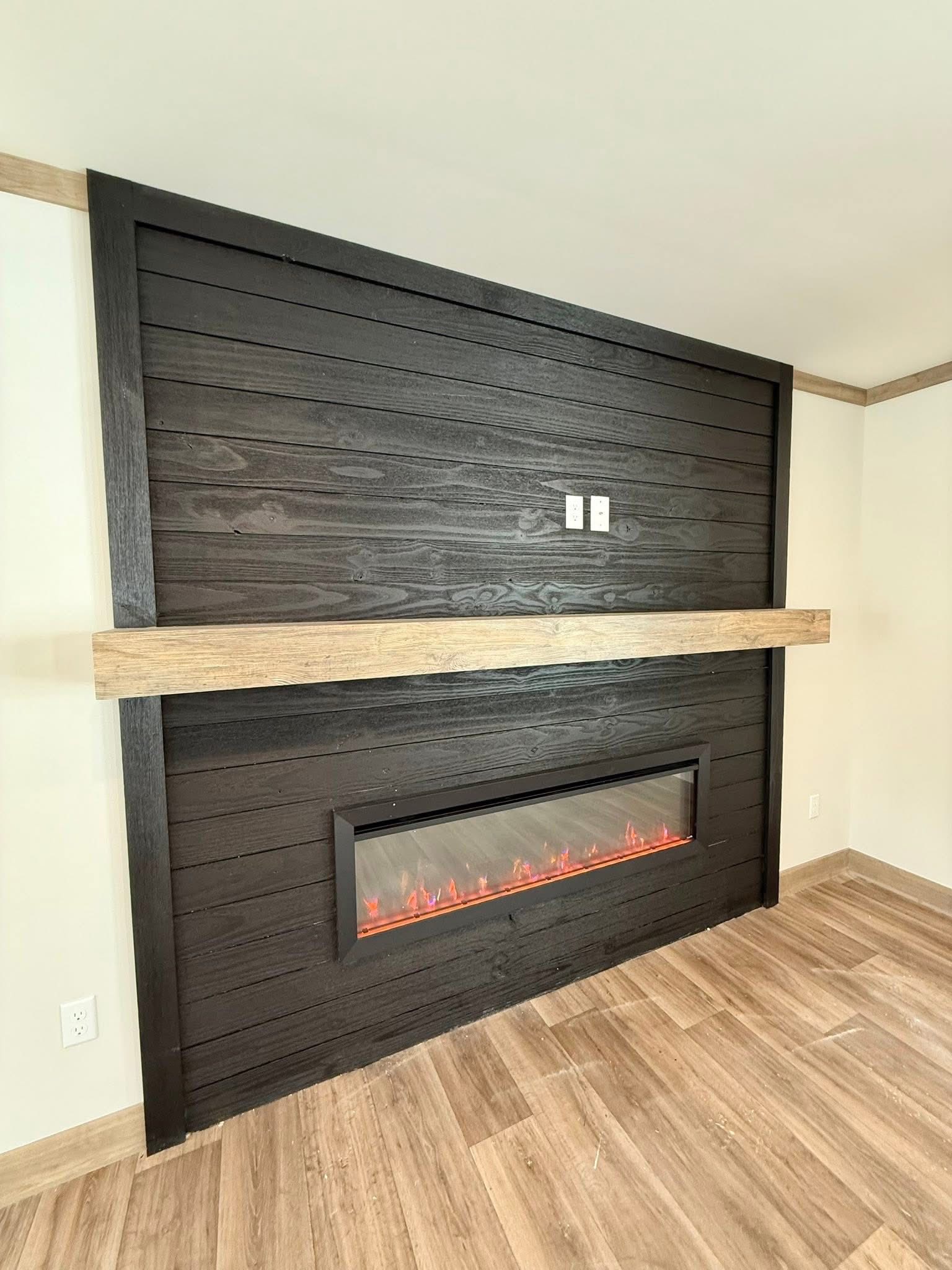 Modern interior with a sleek black shiplap wall, a light wood accent beam, and a recessed electric fireplace emitting a warm glow, atop a wood-patterned floor.