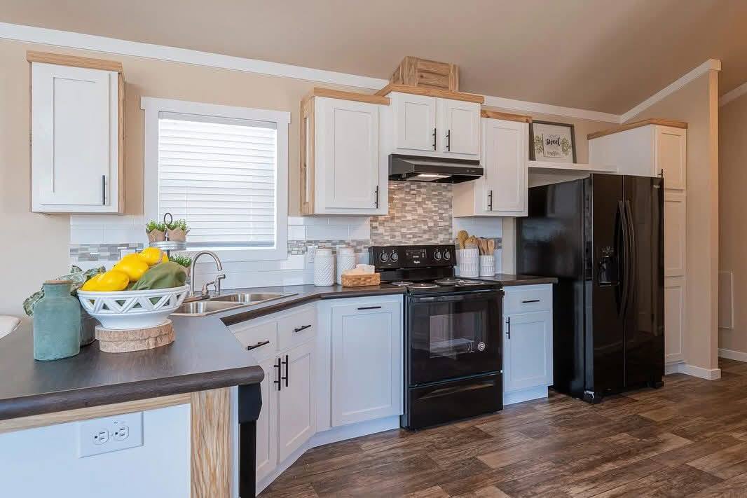 Modern kitchen with white cabinets, black appliances, and wood accents. A bowl of lemons adds a touch of color on the dark countertop.