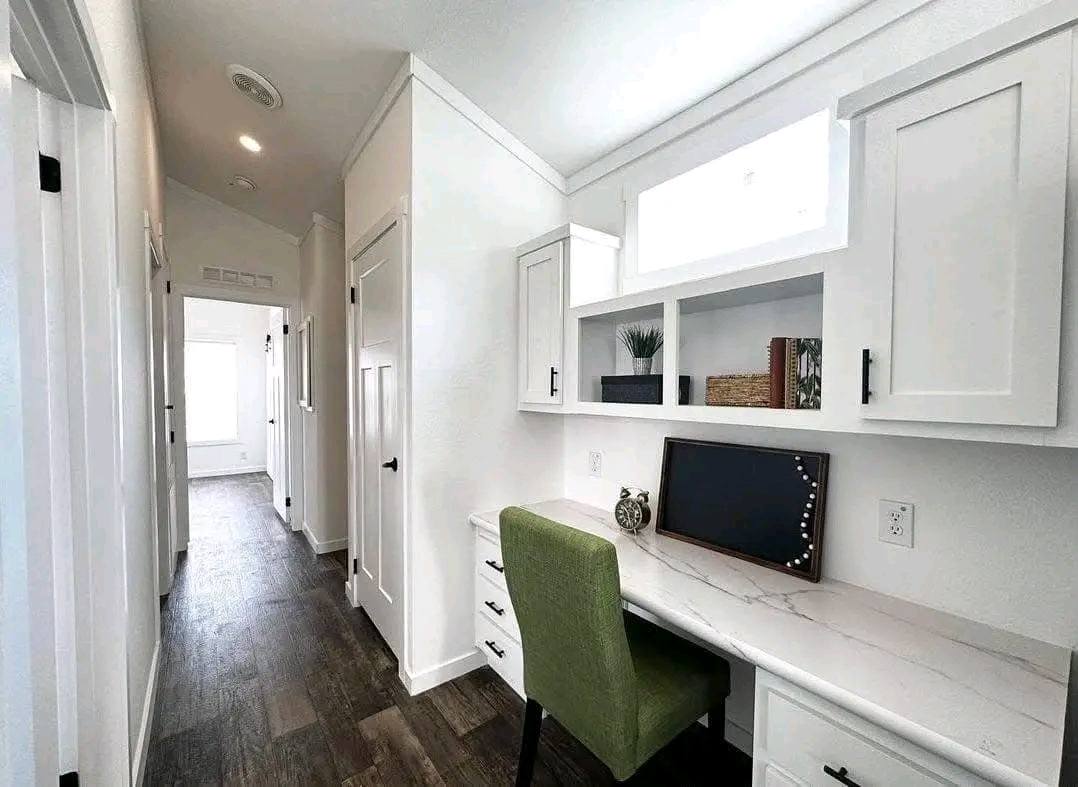 Bright hallway with white walls and wood flooring, featuring a built-in desk with marble top. It includes a green chair and decorative items.