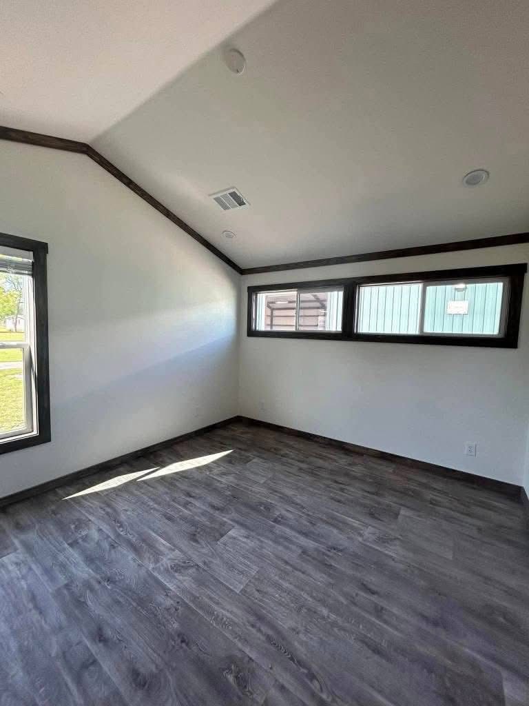 Modern room with vaulted ceiling and dark wood flooring. Natural light streams through two windows, creating a bright, airy atmosphere.