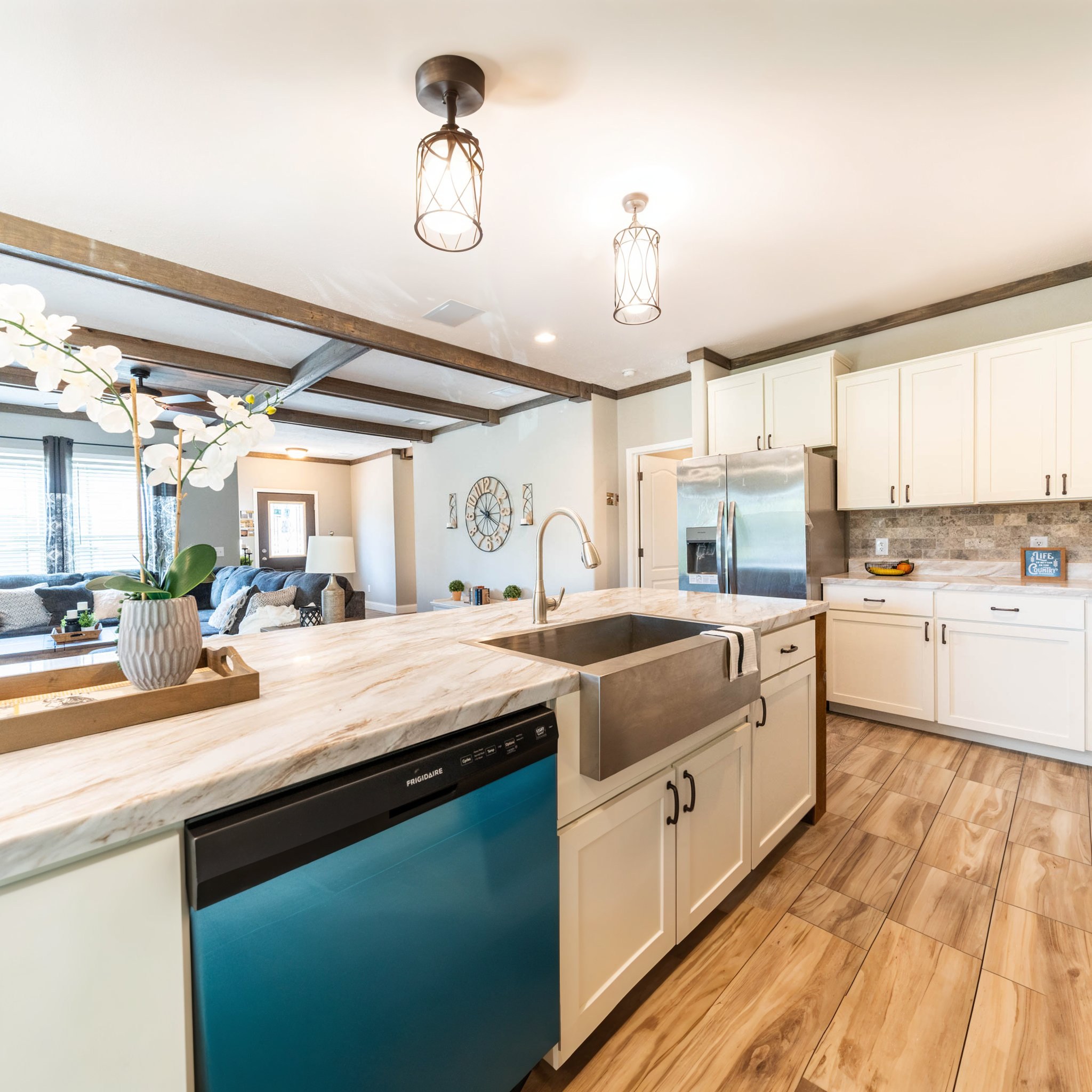 Spacious kitchen with white cabinets, wood floors, and stainless steel appliances. Marble countertop features a vase with white flowers. Modern and inviting.