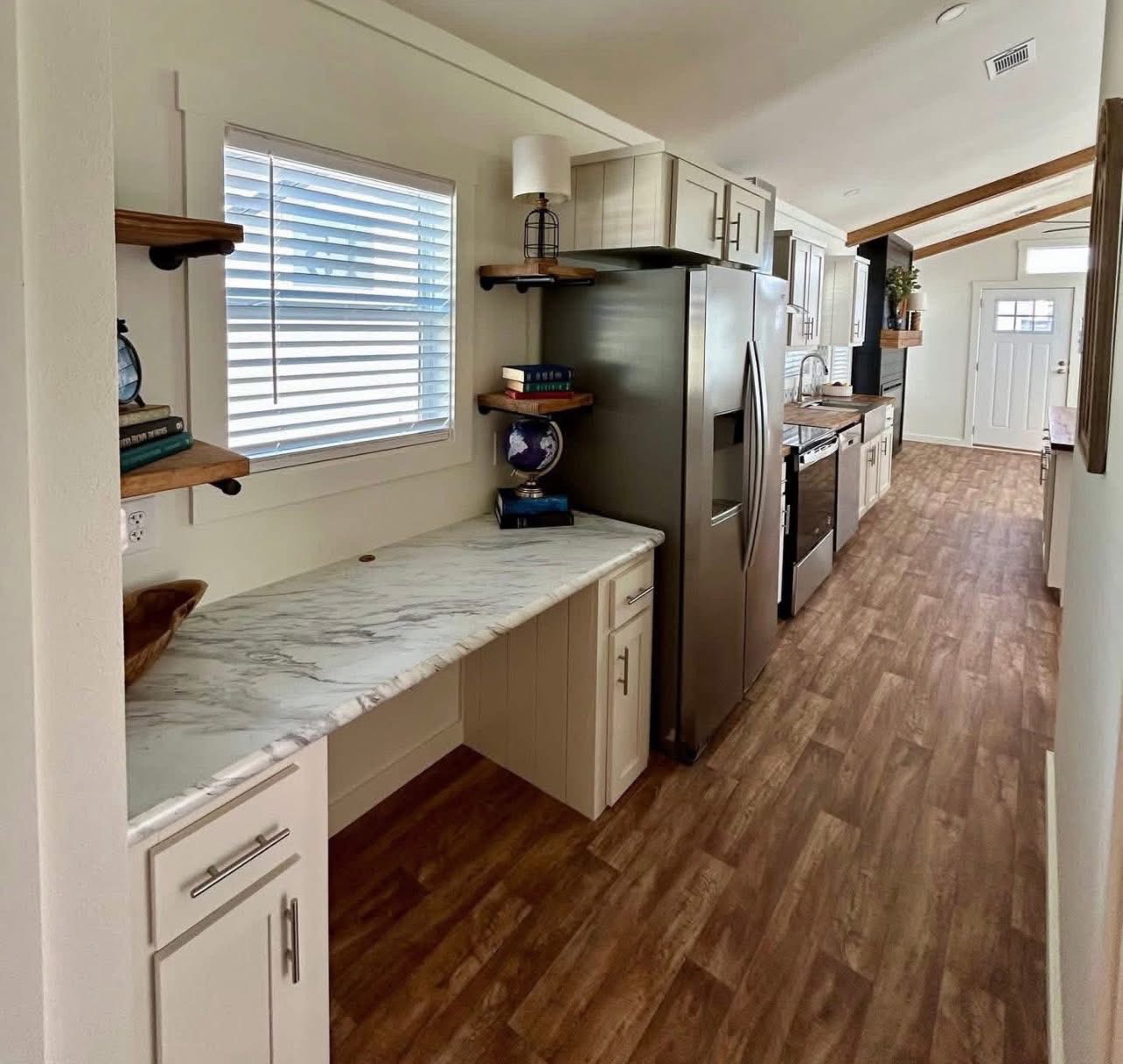 Modern galley kitchen with wooden floor, marble countertops, stainless steel appliances, and open shelves. Bright and spacious with a cozy feel.