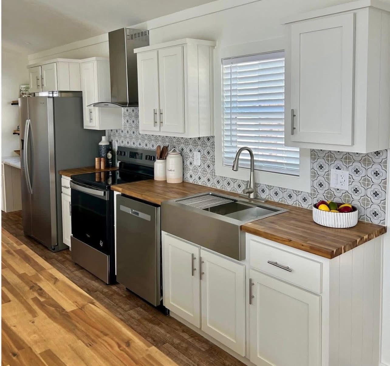Modern kitchen with white cabinets, wooden countertops, and stainless steel appliances. Decorative backsplash with geometric tiles and a fruit bowl adds warmth.